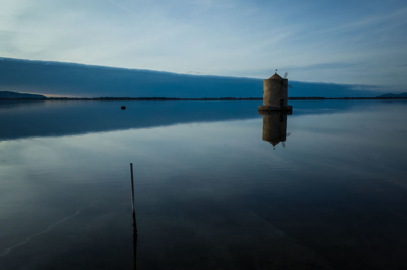 Traditional windmill in lake against sky during sunset