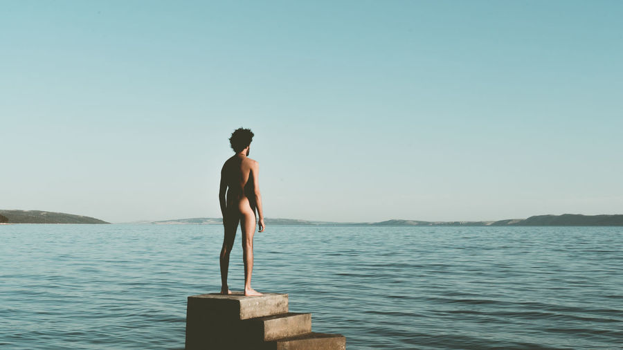 Naked man standing on steps at beach against sky