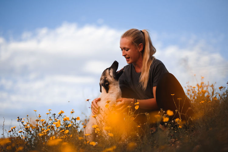 Young woman with dog on field against sky