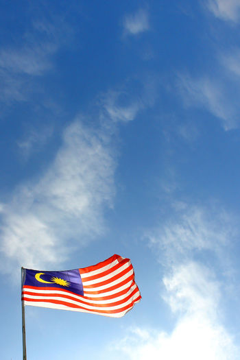 Low angle view of malaysian flag waving against blue sky