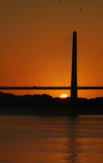 Silhouette bridge against orange sky during sunset