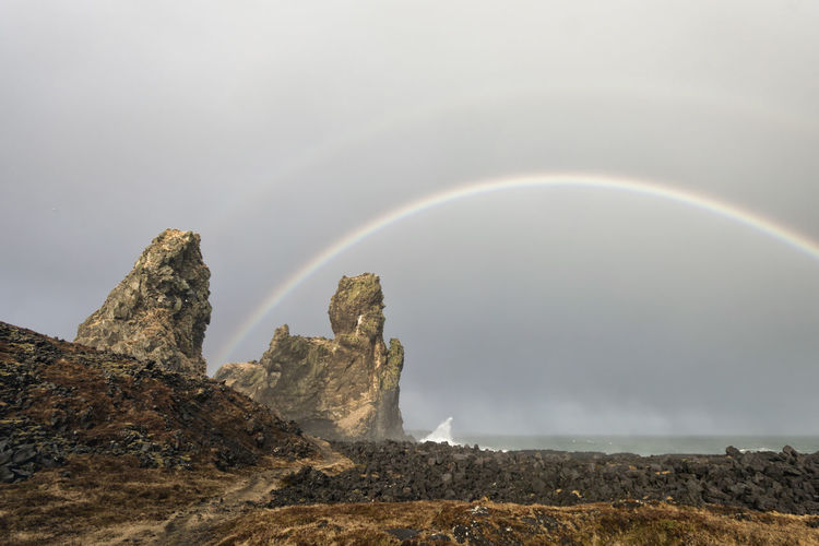 Rock formations against rainbow over sea