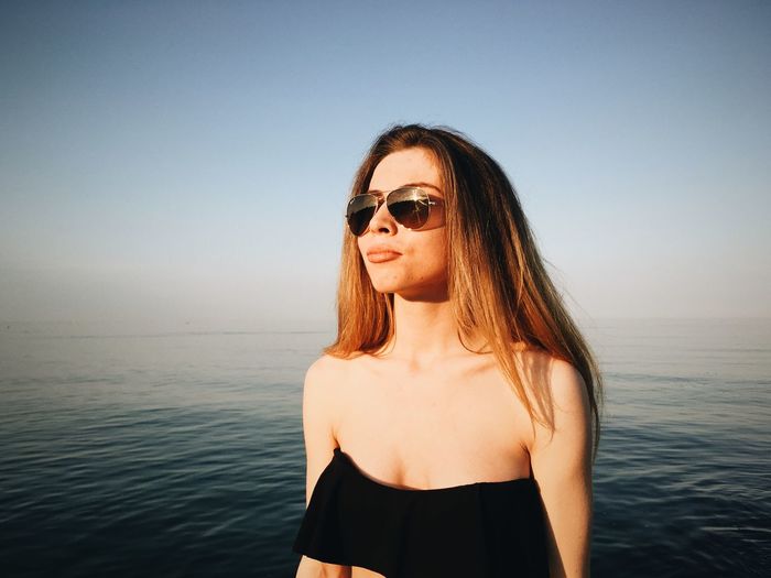 Close-up of young woman wearing sunglasses at sea against clear sky