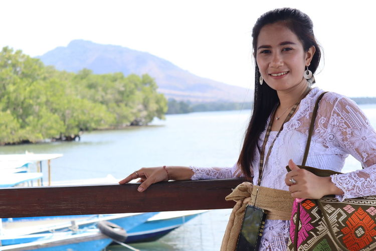 Portrait of smiling woman standing by railing against lake