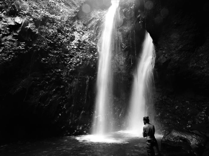 Rear view of man standing by waterfall in forest