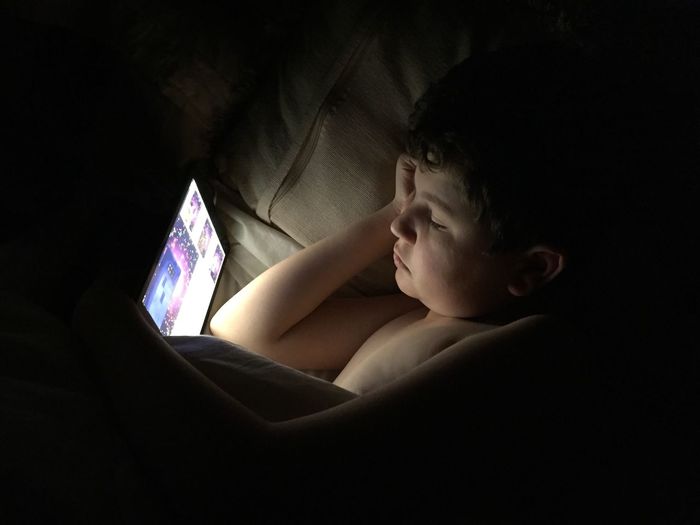 High angle view of boy using digital tablet on bed in darkroom