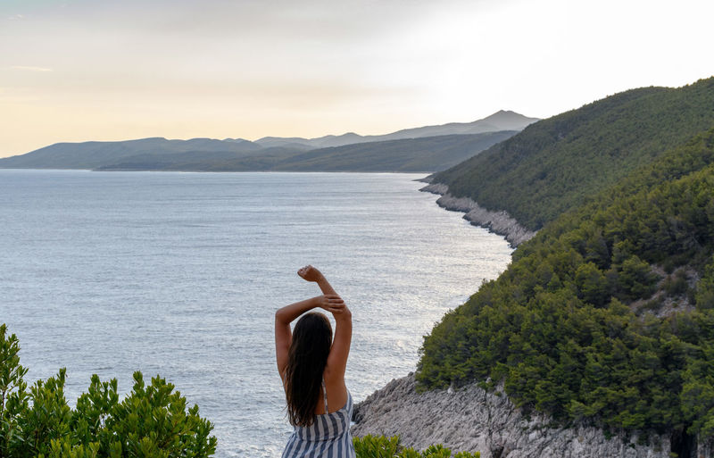 Rear view of young woman standing on lookout point with amazing view of coastline and sea