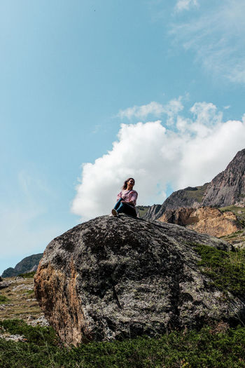 Low angle view of woman sitting on mountain against sky