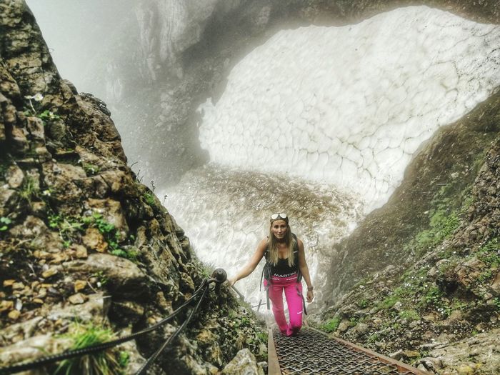 Full length of woman climbing mountain against waterfall