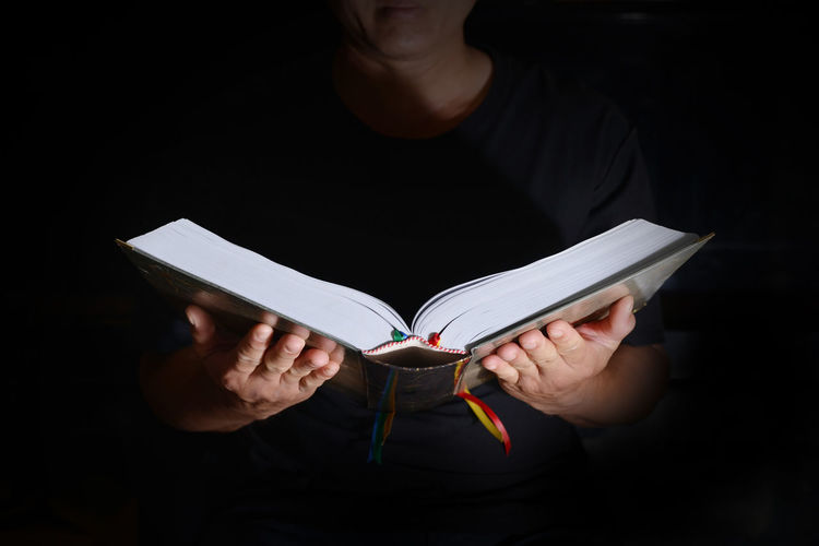 Midsection of woman reading book against black background