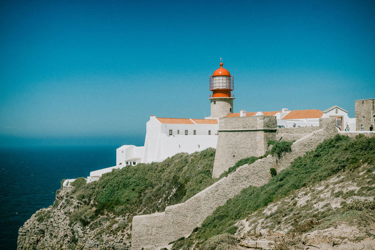 Lighthouse amidst buildings against blue sky