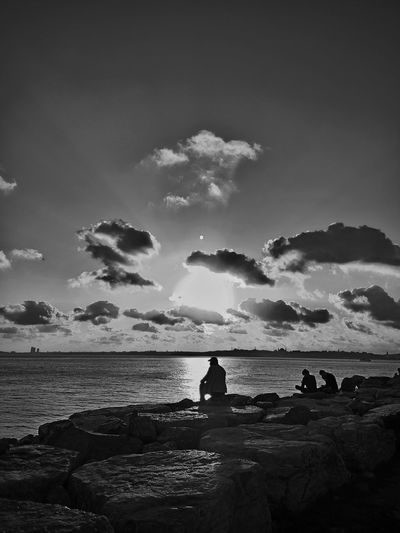 Silhouette of people looking at sea against sky