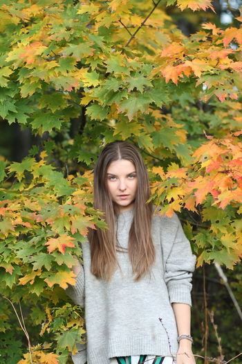 Portrait of beautiful young woman standing in autumn leaves