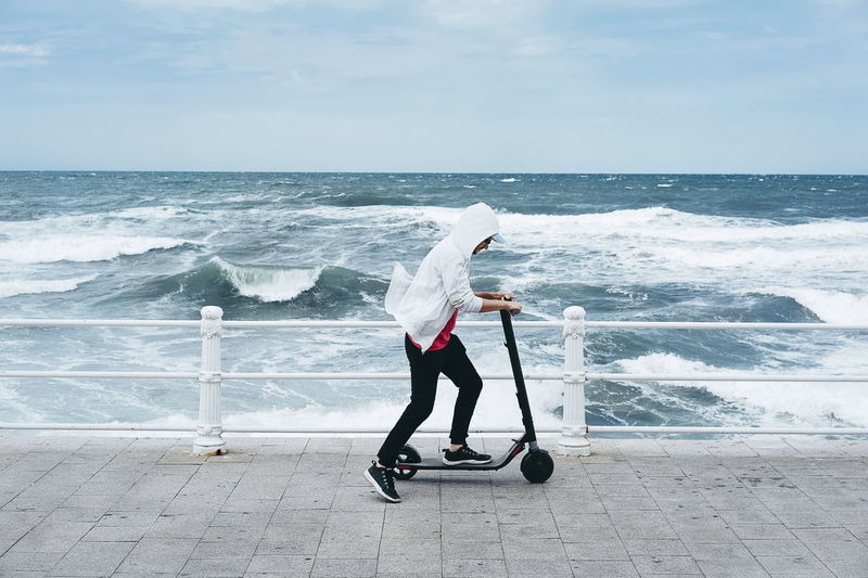 Man riding push scooter at beach against sky