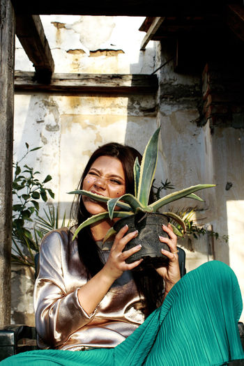 Portrait of smiling young woman eating plant while sitting outdoors