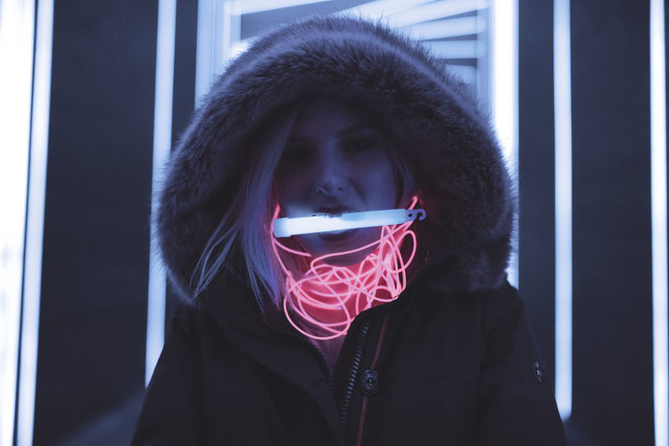 Woman in hooded clothing carrying equipment in mouth standing against illuminated lights
