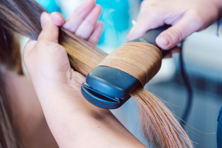Hairdresser straightening hair of woman customer