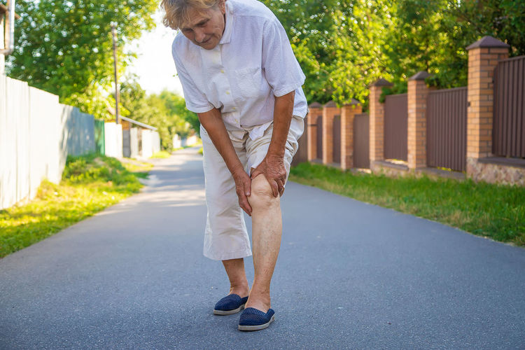 Senior woman touching injured knee on road