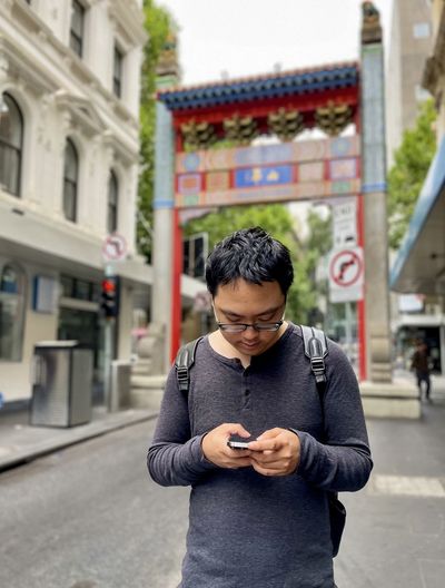 Portrait of asian man using mobile phone against arch and buildings in chinatown-melbourne australia