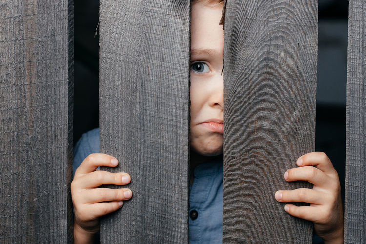 Surprised white boy looks out of the crack of a wooden fence. childish curiosity. espionage. 