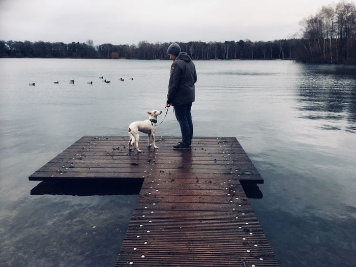 Full length of woman standing with dog on jetty over lake