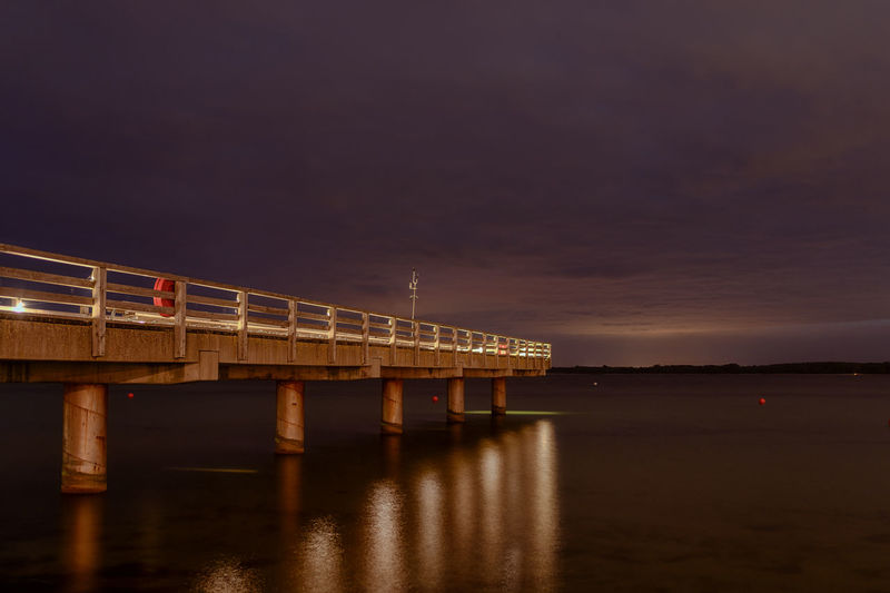 Small illuminated pier at night in the baltic sea with reflective light trails on the water 