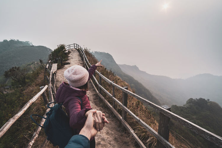 Cropped image man holding woman hand gesturing towards mountains