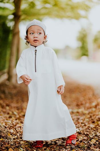 Cute boy standing on leaves covered field during autumn