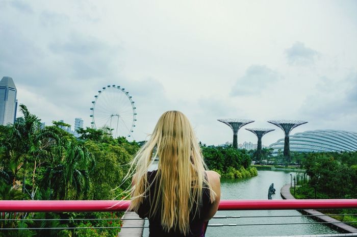 Rear view of woman standing by railing against cloudy sky