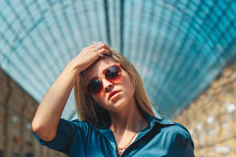 Portrait of young woman wearing sunglasses against ceiling