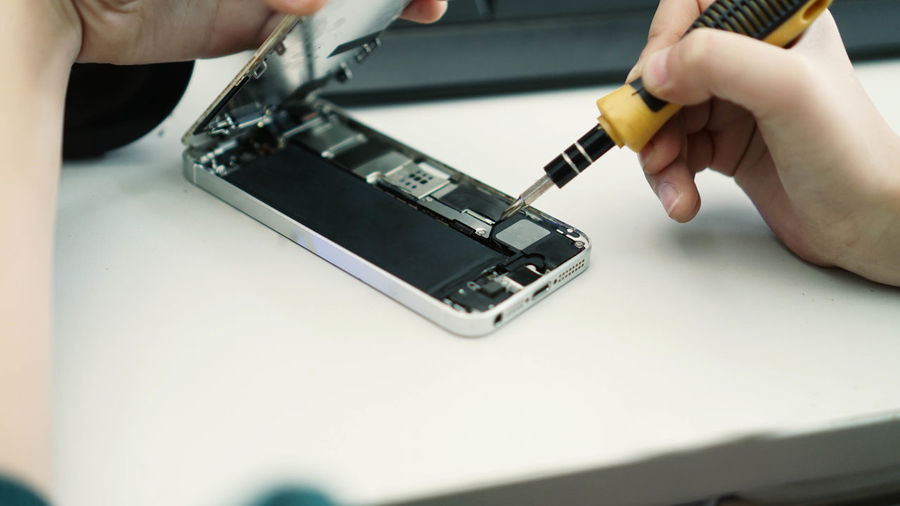 Cropped hands repairing mobile phone on table