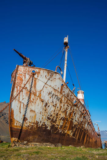 Low angle view of abandoned ship against clear blue sky