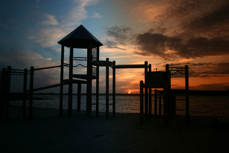 Silhouette built structure on beach against sky during sunset