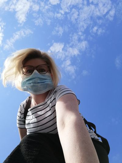 Low angle portrait of woman wearing mask against sky
