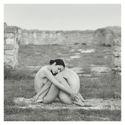 Side view of naked women embracing while sitting on field
