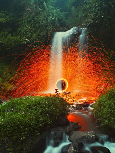 Man standing by wire wool against waterfall in forest