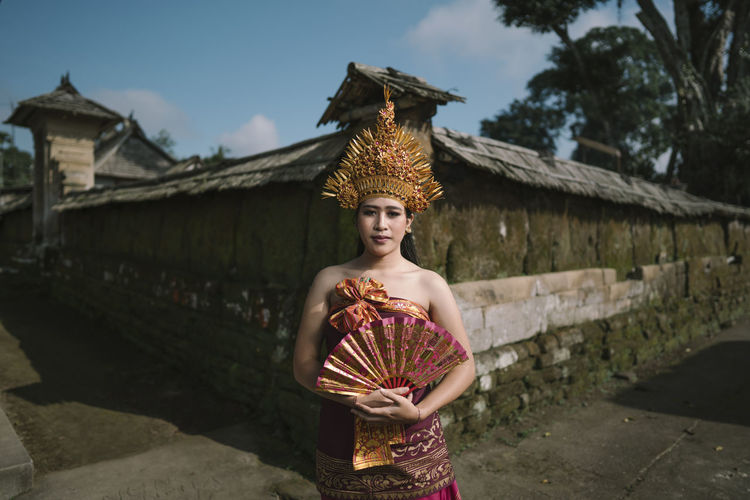 Portrait of young woman wearing traditional clothing while standing with hand fan