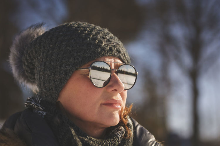 Close-up of woman in warm clothing wearing sunglasses against bare trees