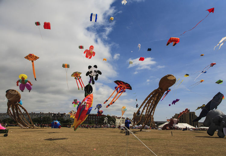 Low angle view of people flying kites against a cloudy sky on a sunny day at southsea kite festival. 