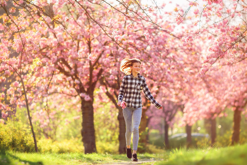 Full length of woman standing by pink flowers in park