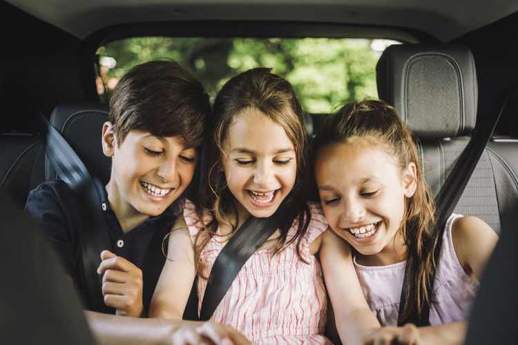 Happy male and female siblings wearing seat belt while enjoying in car
