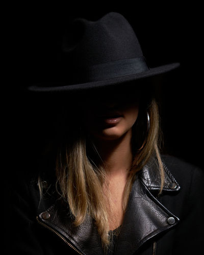 Close-up of female model wearing hat against black background
