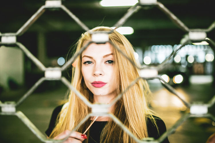 Portrait of beautiful young woman seen through chainlink fence in basement
