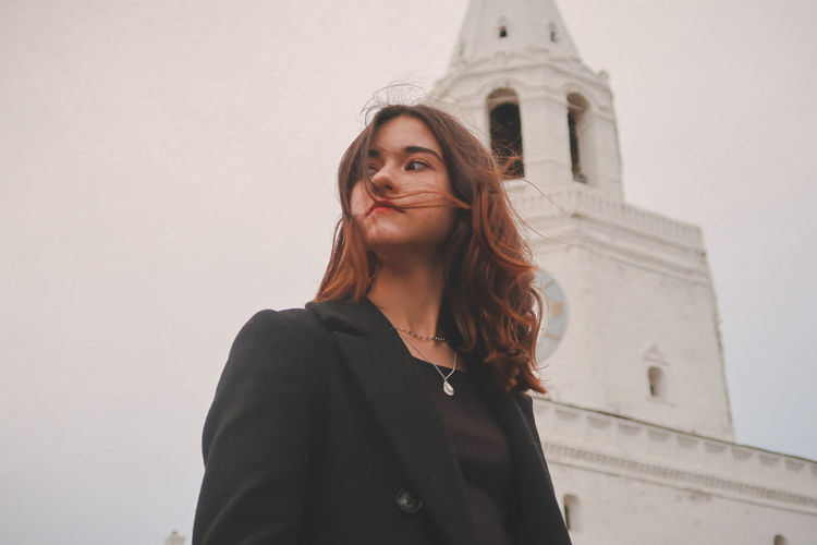Portrait of young woman standing against building