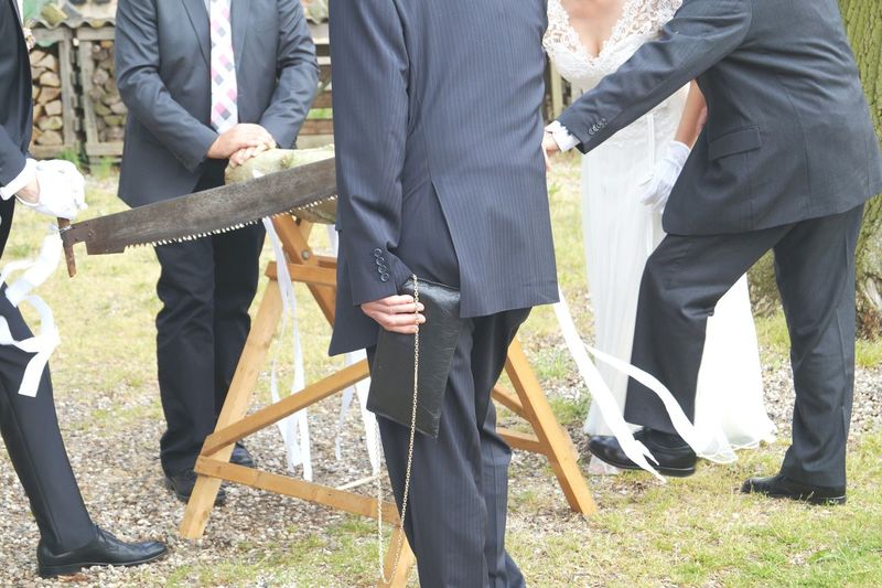 Men in suits with bride holding saw and log on field