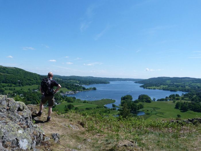 Rear view of man looking at lake windermere against blue sky