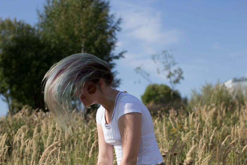 Woman tossing hair while standing on field against sky
