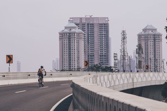 Rear view of man riding bicycle on bridge in city