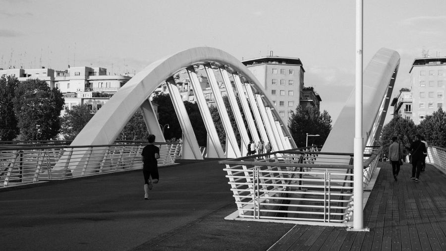 People walking on bridge in city against sky