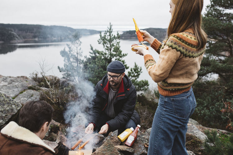 Friends preparing hotdogs over campfire
